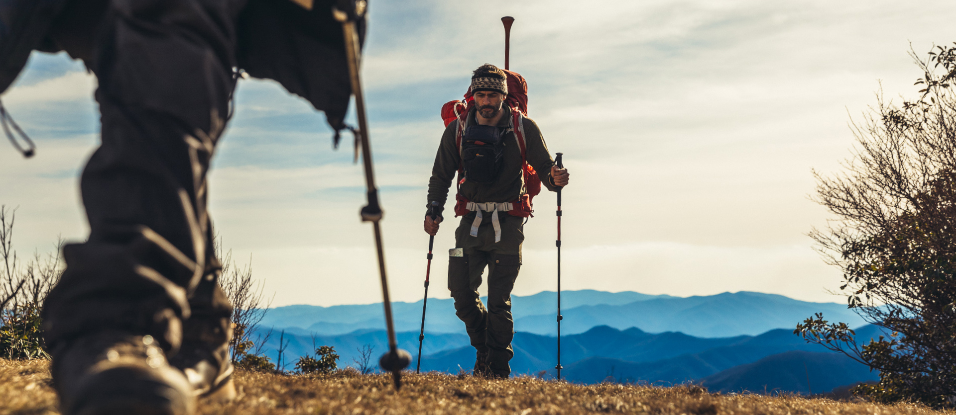 Man hiking up hill following partner with hiking backpack and trekking poles